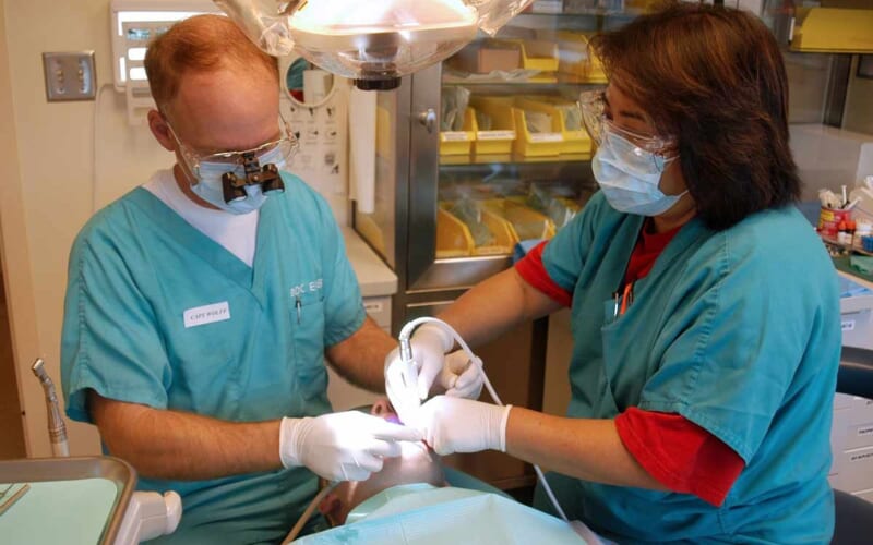 Ein Patient liegt auf einem Zahnarztstuhl, neben ihm ein Zahnarzt und eine Praxishelferin