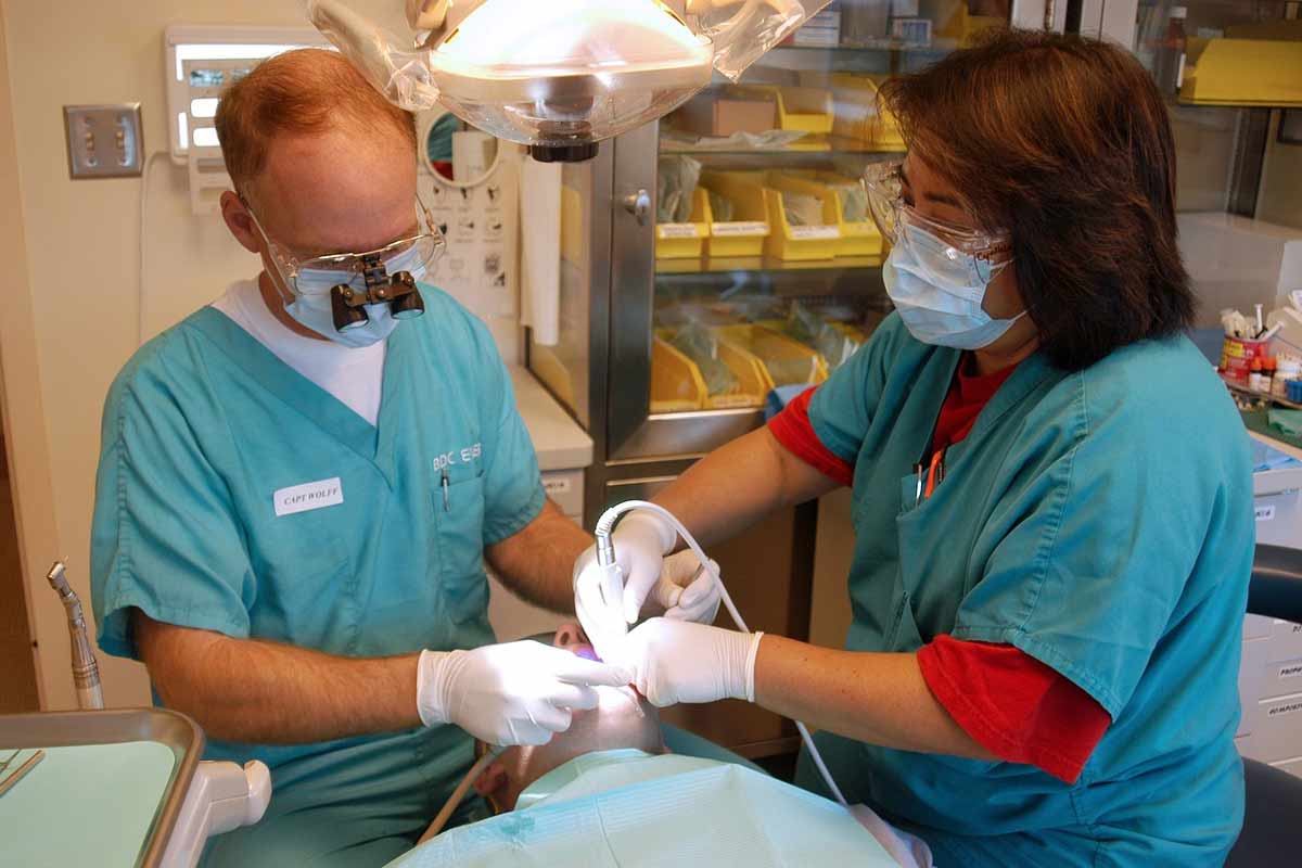 Ein Patient liegt auf einem Zahnarztstuhl, neben ihm ein Zahnarzt und eine Praxishelferin